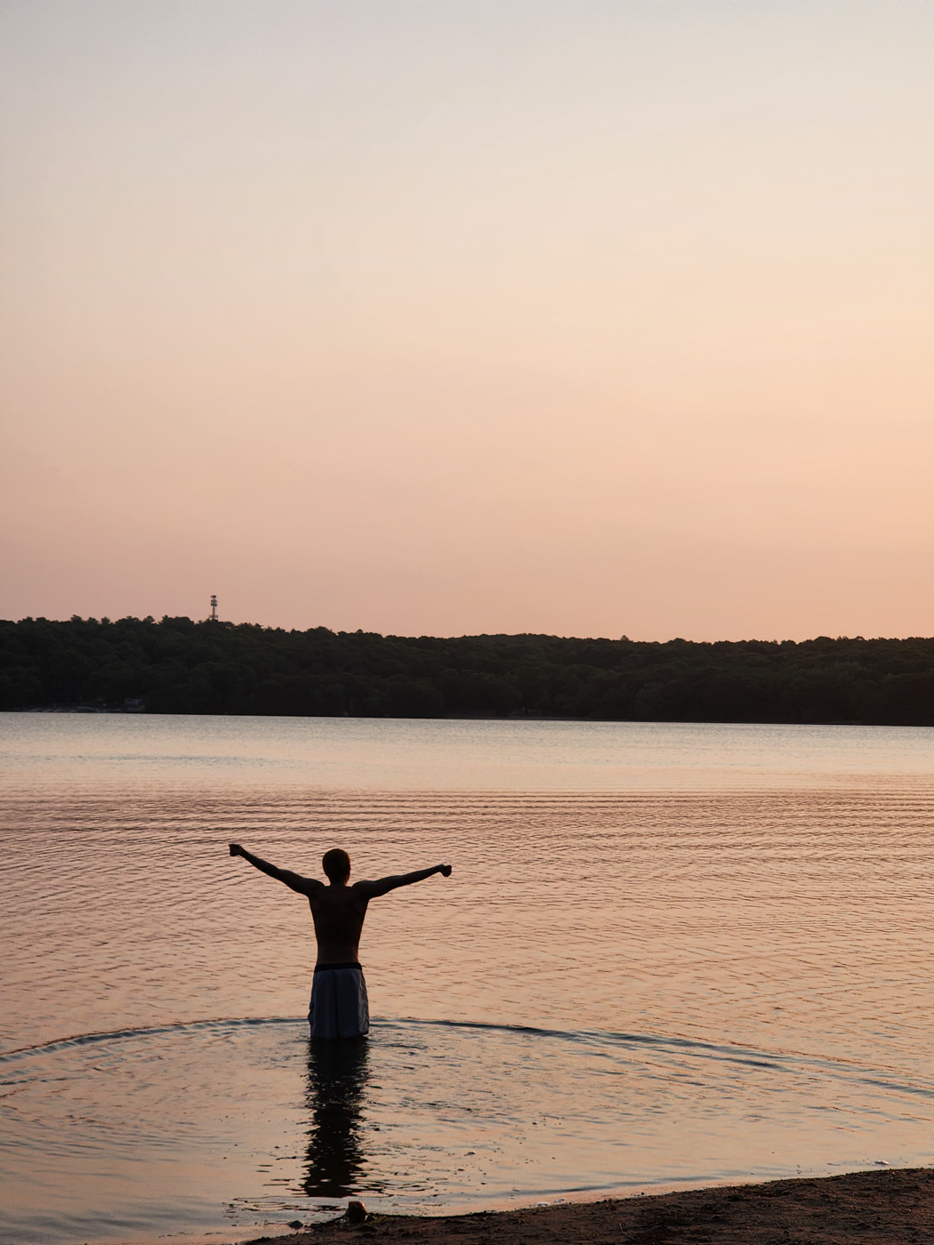 A person standing in a river at sunset, arms raised